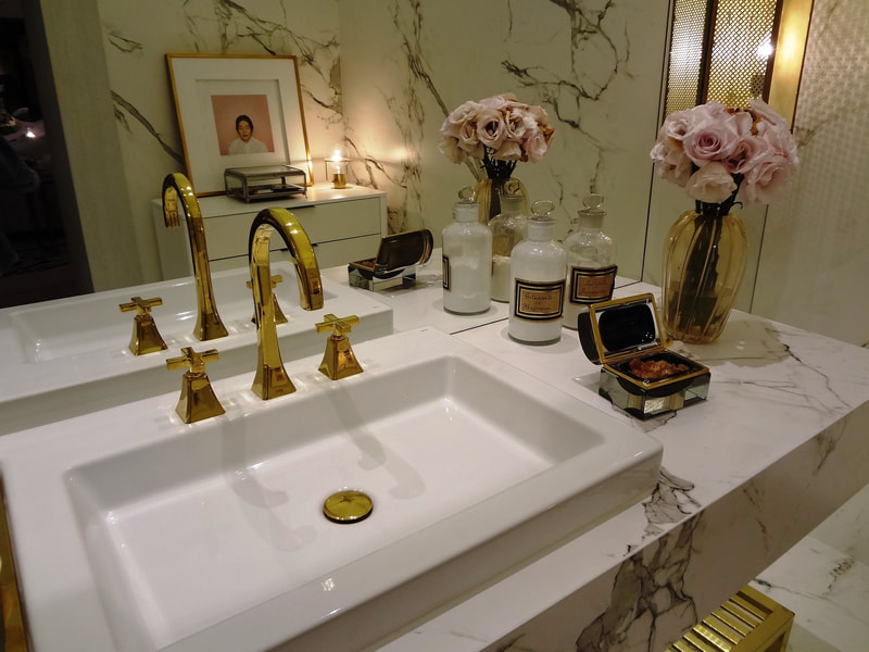 gold-taps-marble-counter-rose-bouquets Luxury bathroom vanity with gold taps, white sink, marble worktop, and vases of pink roses.