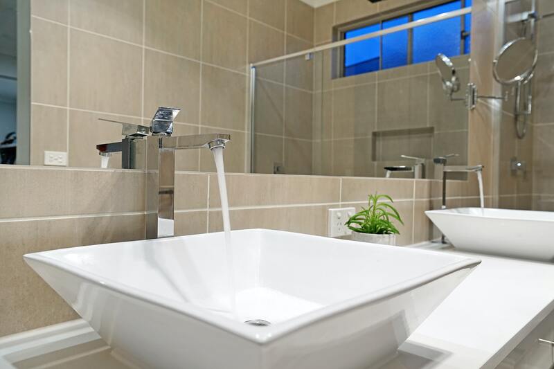 square-vessel-sink-with-running-chrome-tap A close-up of a square white vessel sink with water running from a tall chrome tap, with a shower cubicle reflected in the mirror behind.